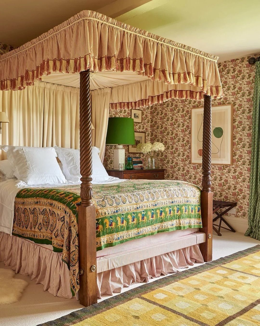 A four-poster bed featuring a ruffled striped canopy and a green patterned quilt in a floral bedroom.