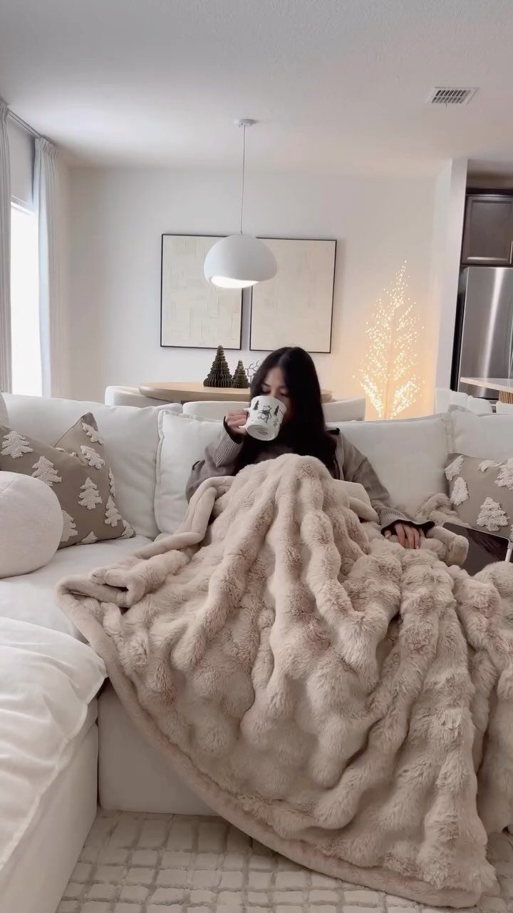A person wrapped in a thick, textured beige faux fur throw blanket on a white sofa.