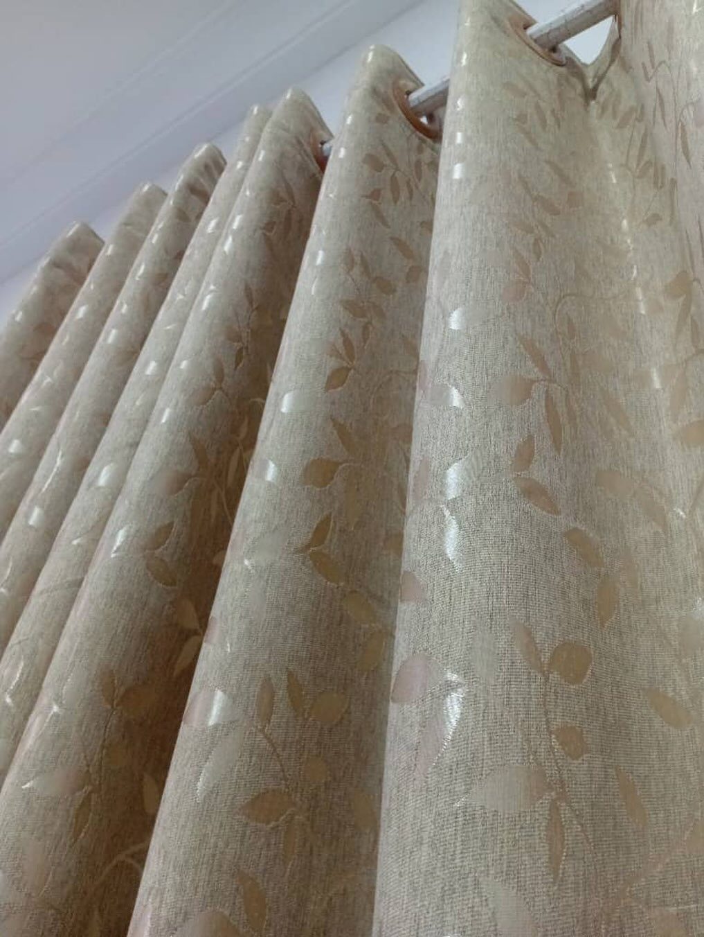 Thick beige curtains with a leaf pattern hanging from a white curtain rod.
