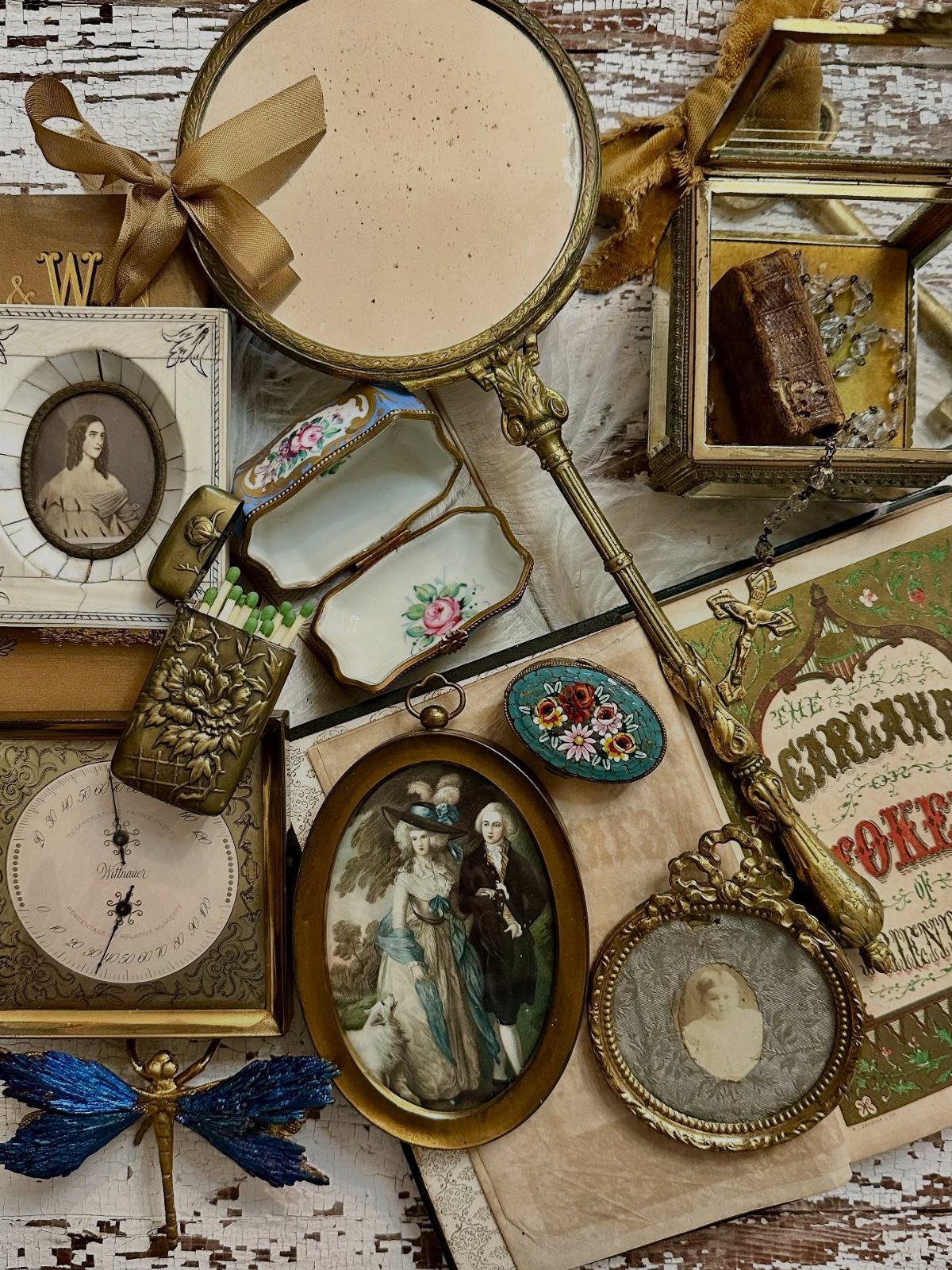 Vintage items including a gold mirror, antique clock, and small portraits on white wood.