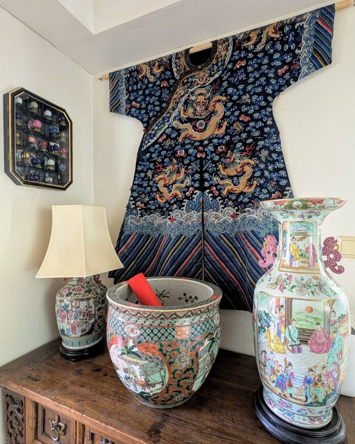 Ornate ceramic vases and an embroidered garment displayed on a wooden dresser.