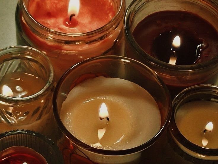 Lit candles in various colored glass jars glowing with warm light.