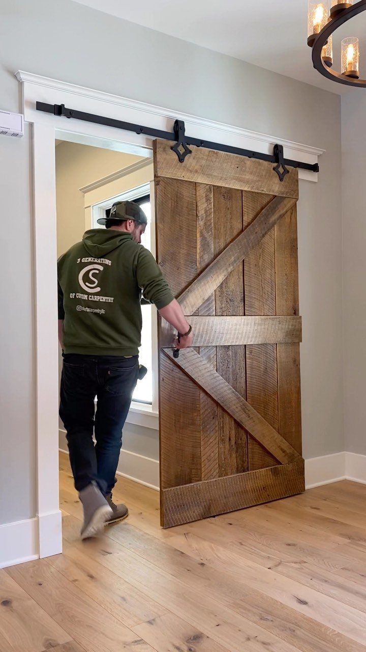 A man sliding a large wooden farmhouse style barn door along a black metal track.