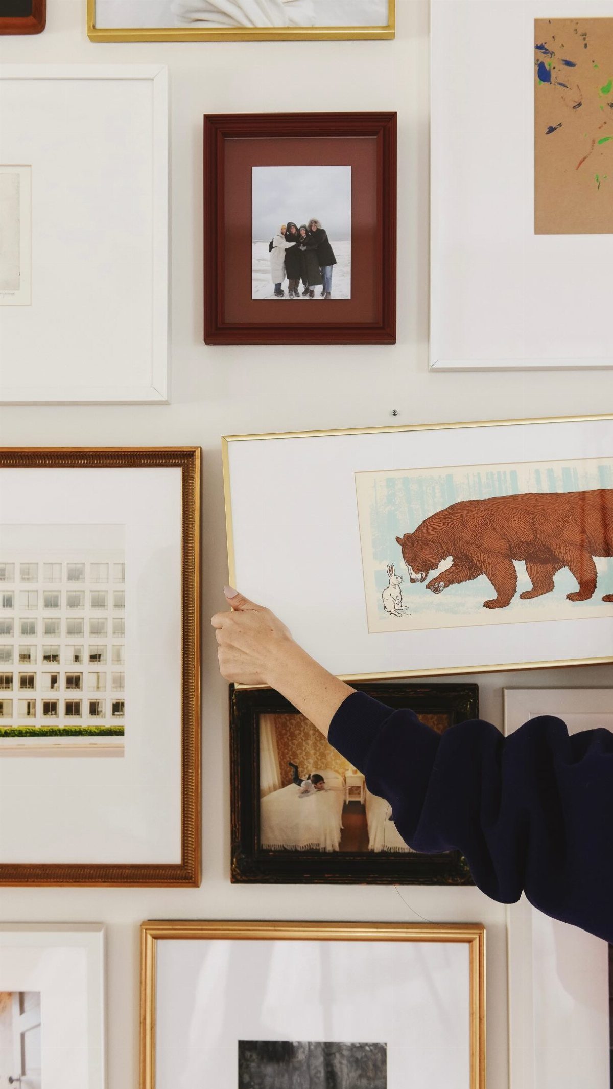 A person hangs a large framed bear illustration onto a white gallery wall.