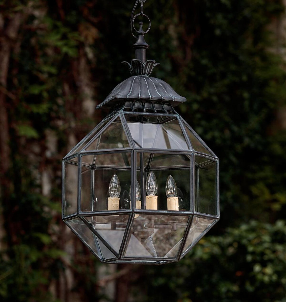 A dark metal hanging lantern with glass panels and small bulbs suspended outdoors.
