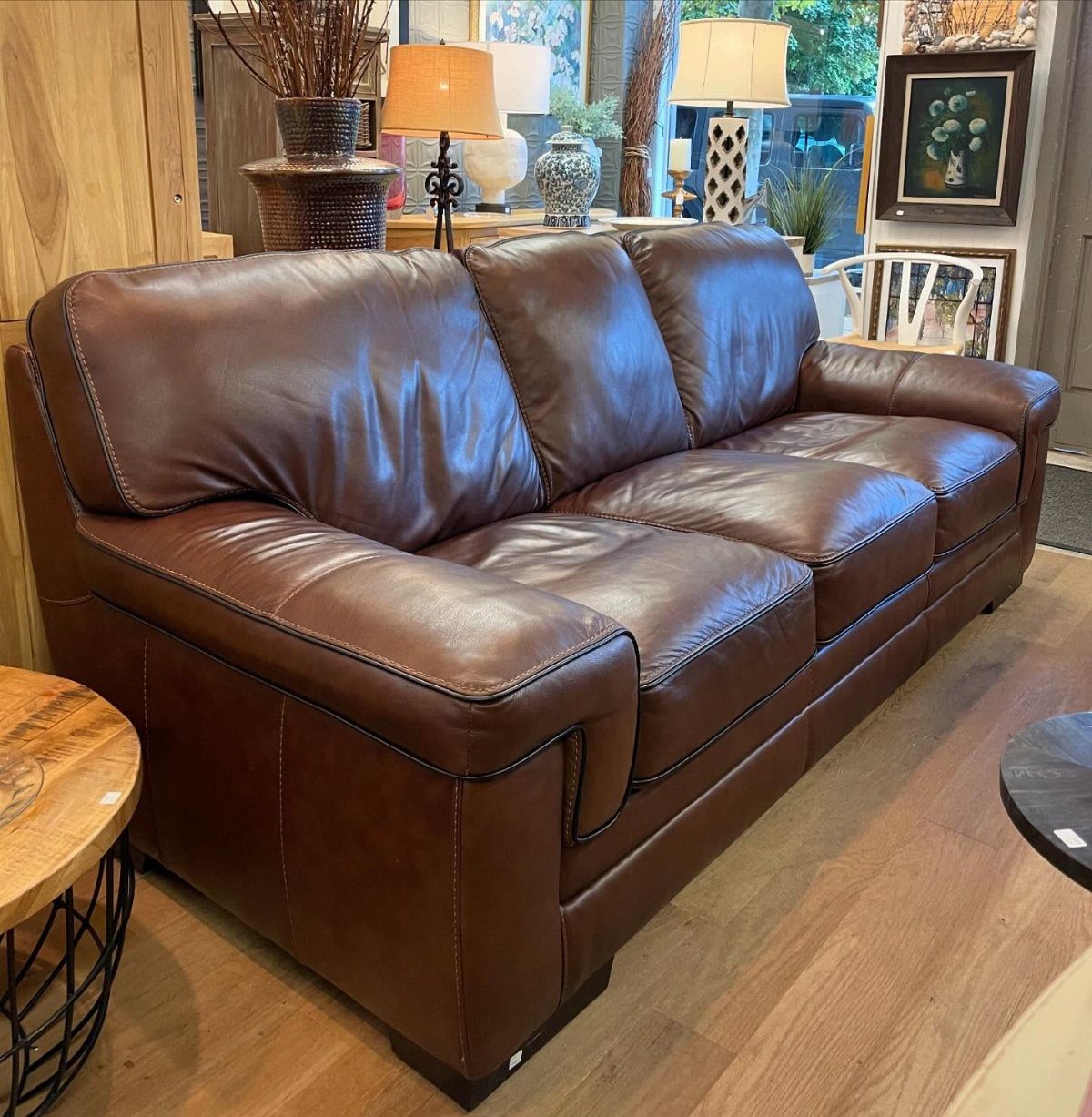 A large brown leather sofa positioned on a light wooden floor in a decorated room.
