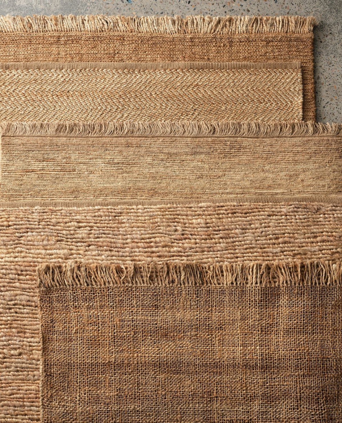 Layered natural fiber rugs with various textures and frayed edges in earthy tan tones.