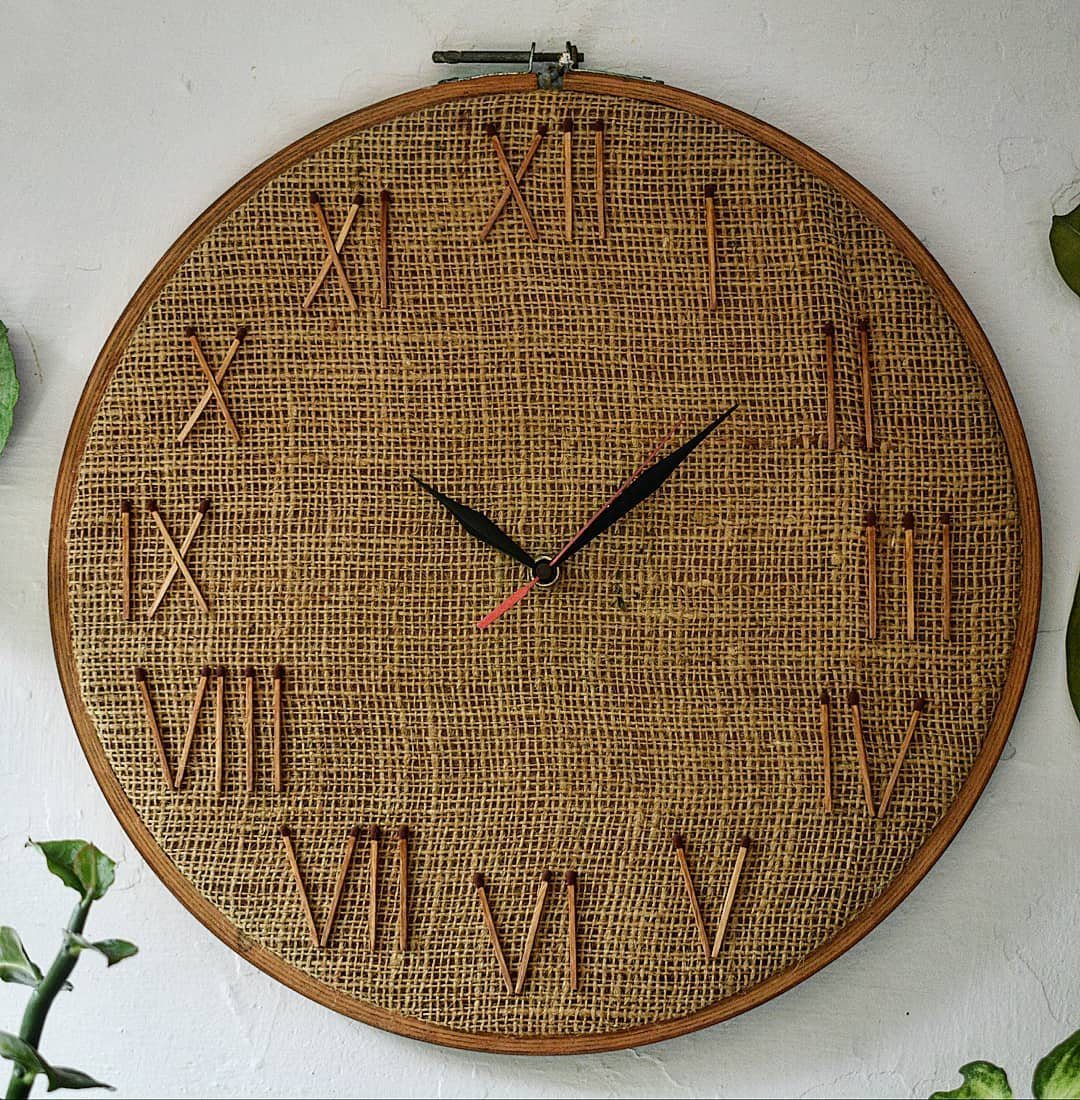 A large rustic wall clock with a burlap face and wooden Roman numerals.