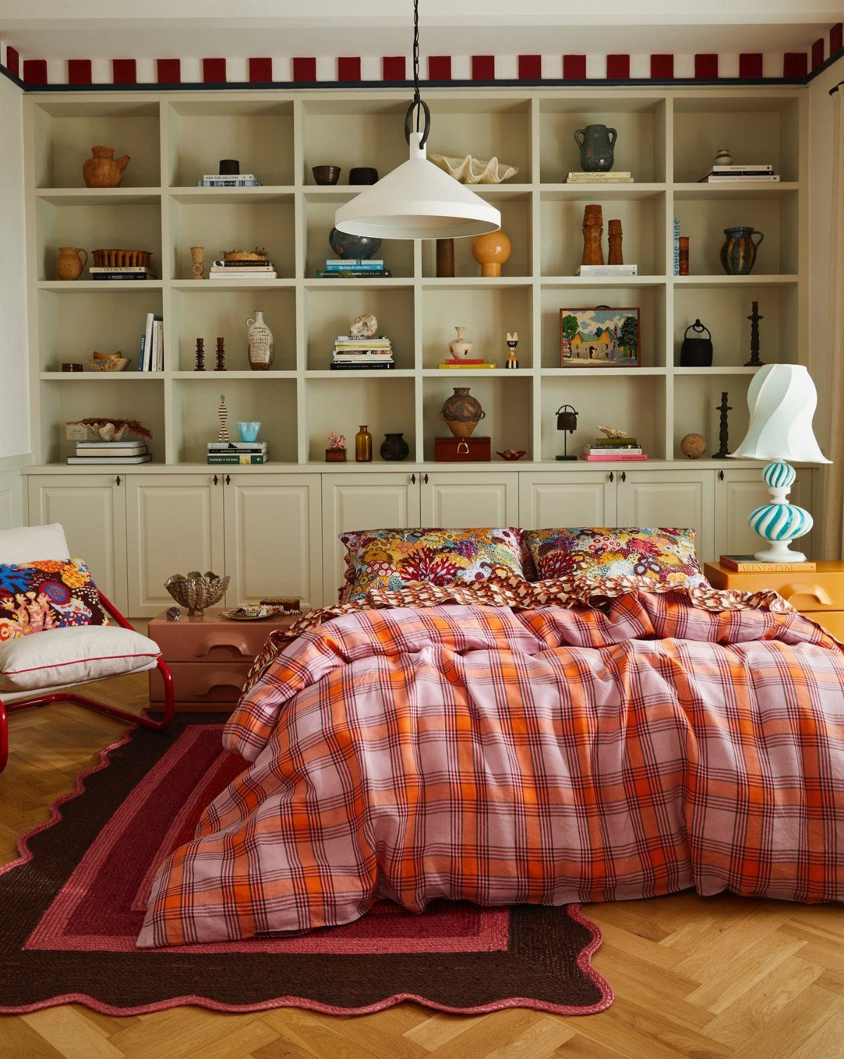 A bed with vibrant orange and purple plaid bedding set against a large white built-in bookshelf.