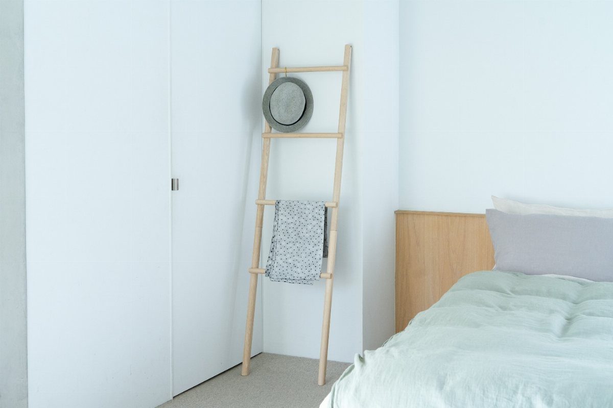 A light wood ladder leaning against a white wall used as a rack for a hat and towel.