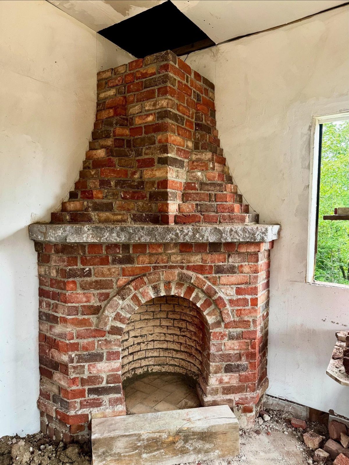 A large red brick fireplace with an arched opening set against a white wall.