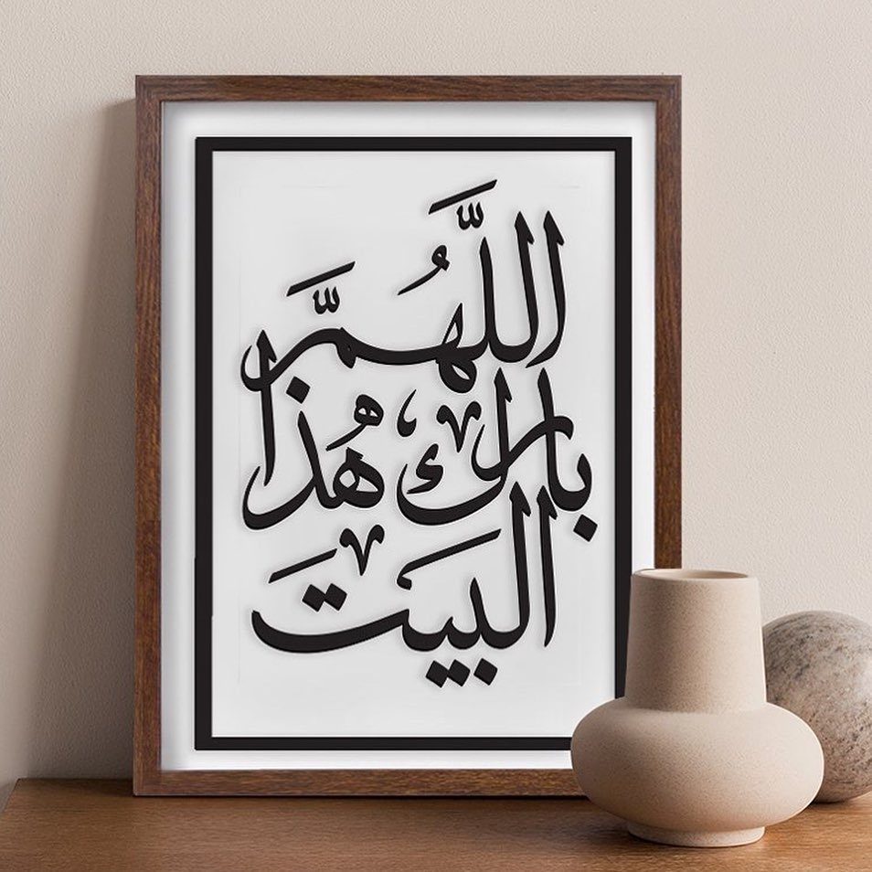 Framed Arabic calligraphy art in a wooden frame sitting on a wooden surface with ceramic vases.