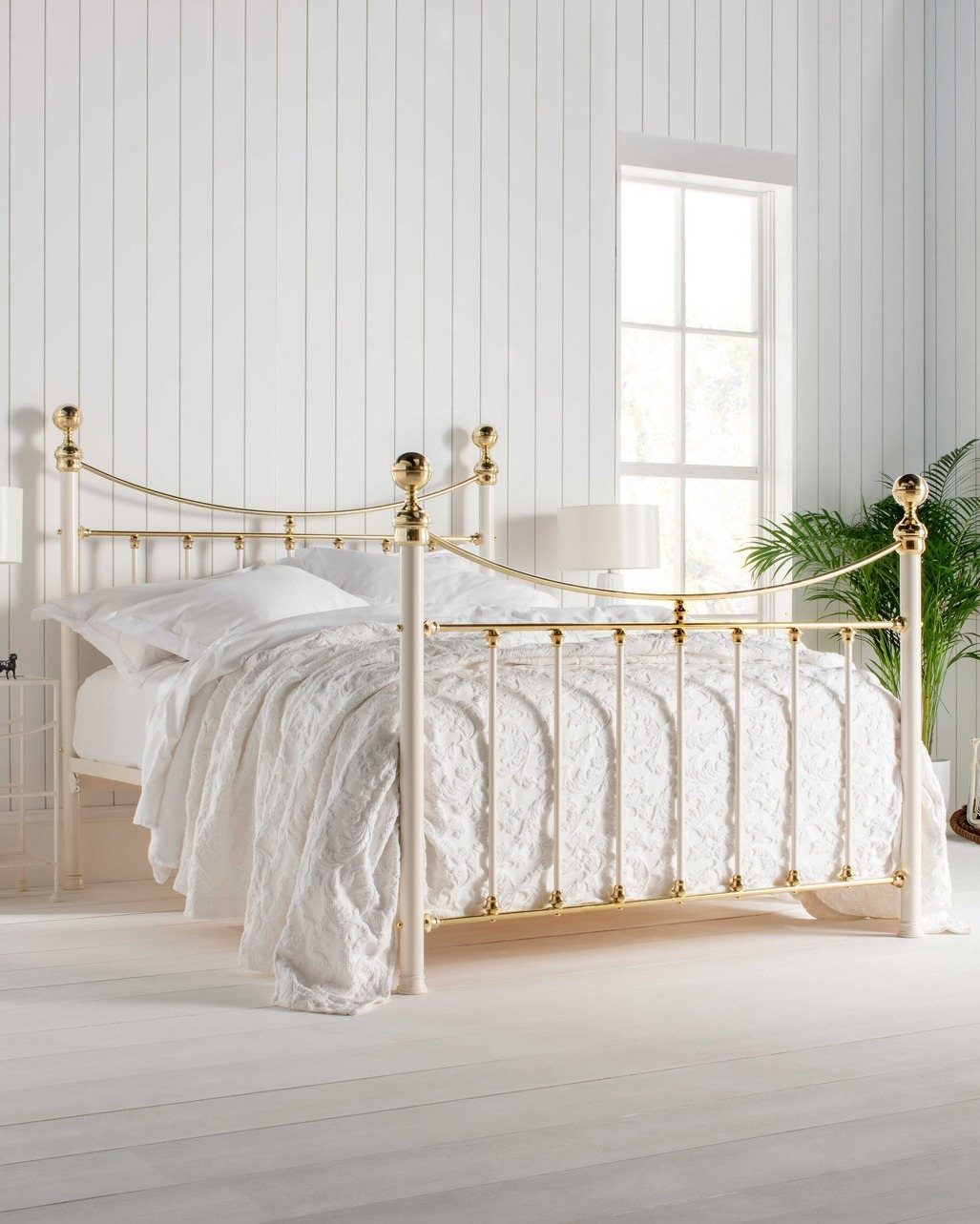 White wrought iron bed frame with gold accents in a bright, white paneled bedroom.