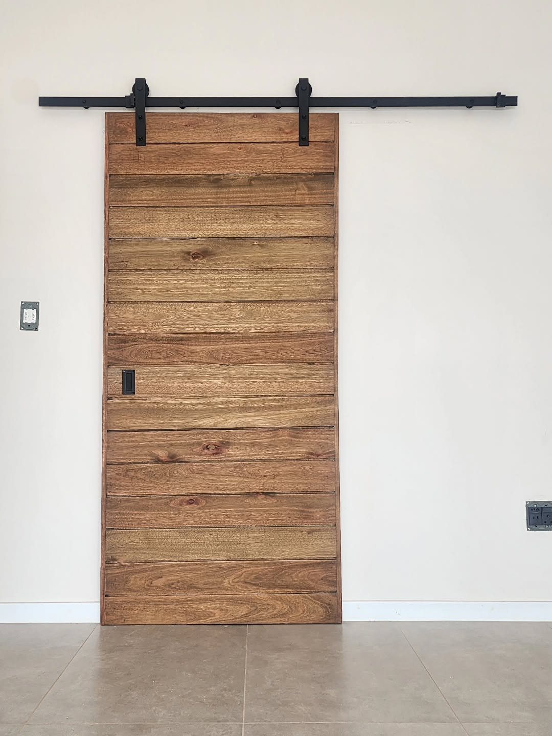 A rustic wooden barn door with black metal hardware mounted on a light wall.