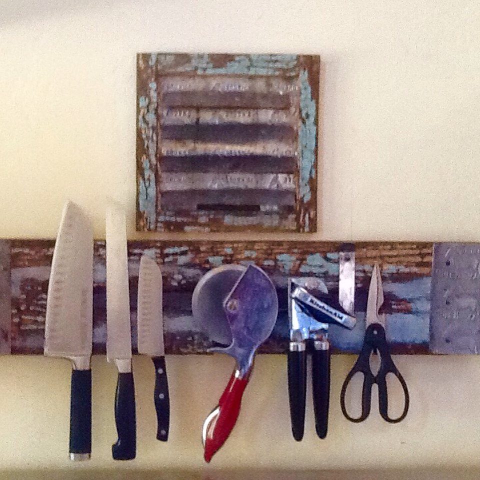 Metal kitchen knives, a pizza cutter, and scissors hanging from a rustic wooden magnetic rack.