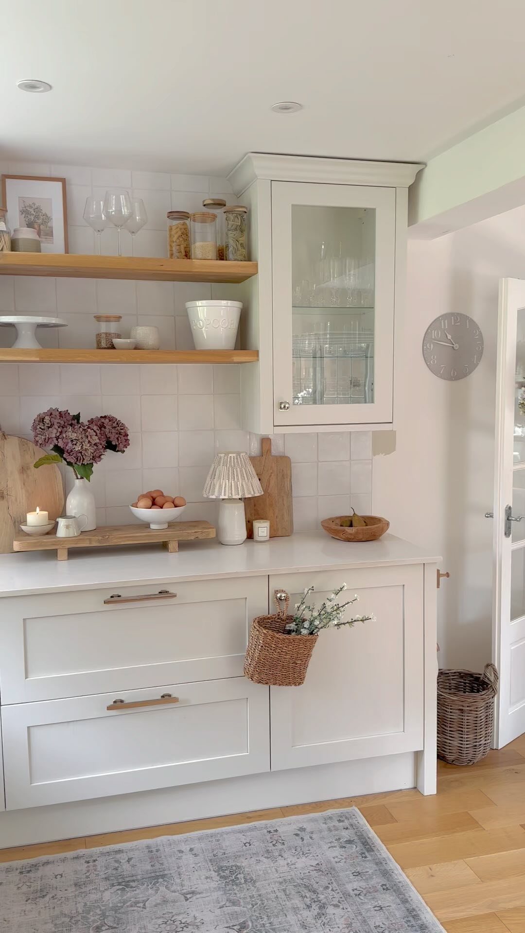 Wooden open shelves holding glass jars and white ceramics against a white tiled wall.