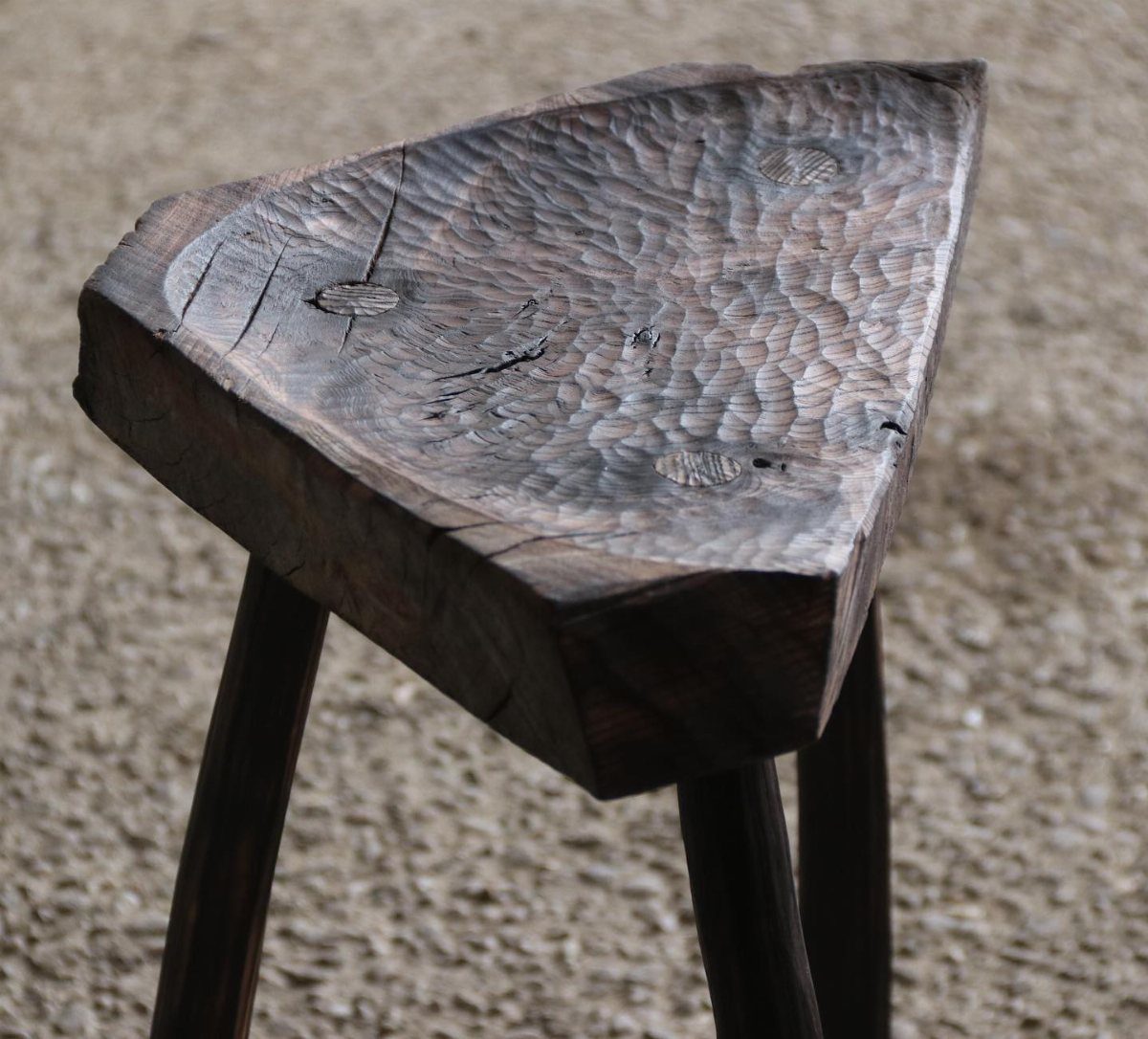 A hand-carved triangular wooden stool with dark legs on a textured rug.