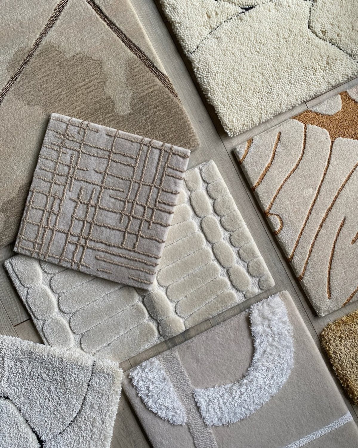 Various textured rug samples in neutral beige and cream tones arranged on a wooden floor.