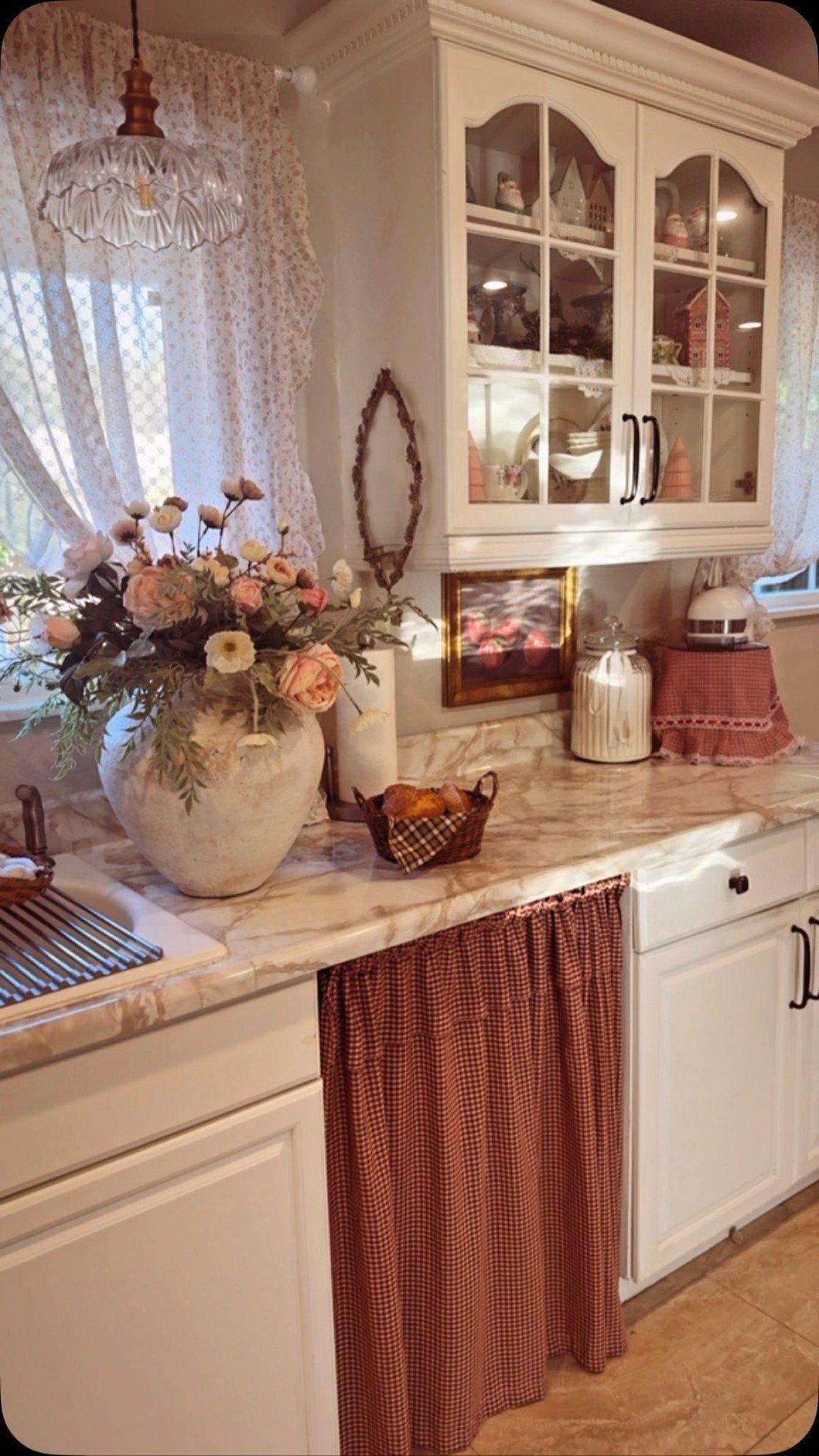Peach flowers in a stone vase sit on a marble countertop near white cabinets.