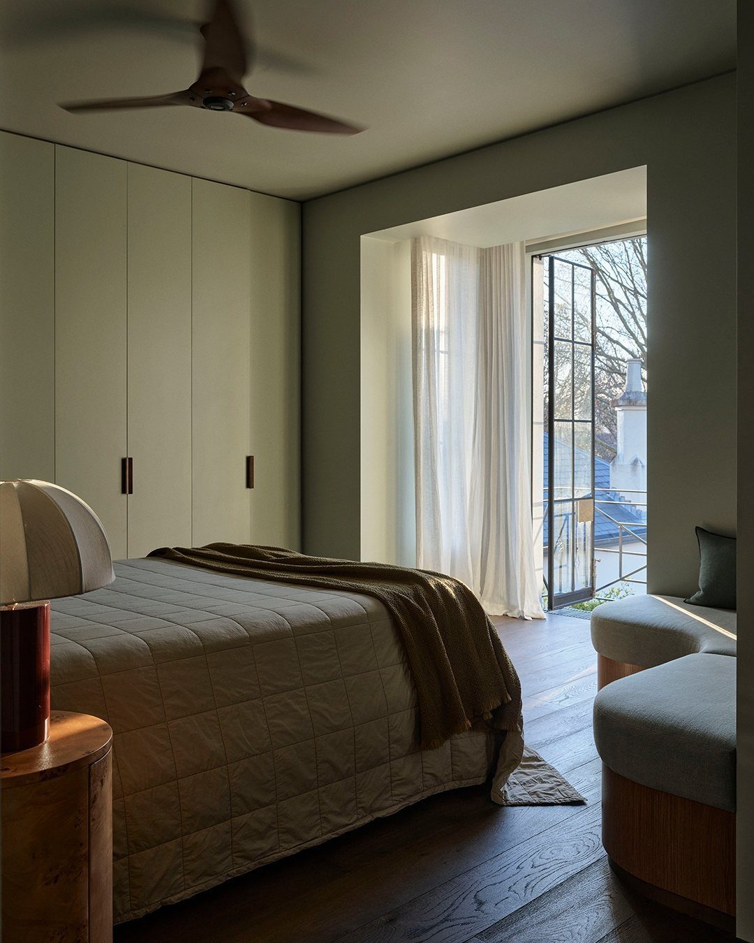 Sage green bedroom with a large bed, built-in wardrobes, and a balcony door with sheer curtains.