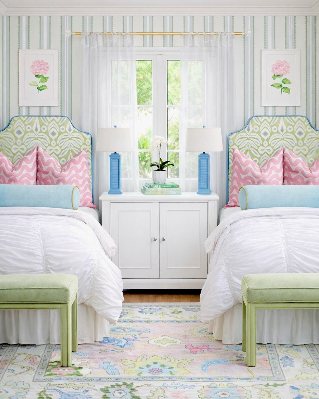 Two twin beds with sage green headboards, pink pillows, and blue accents in a pastel bedroom.