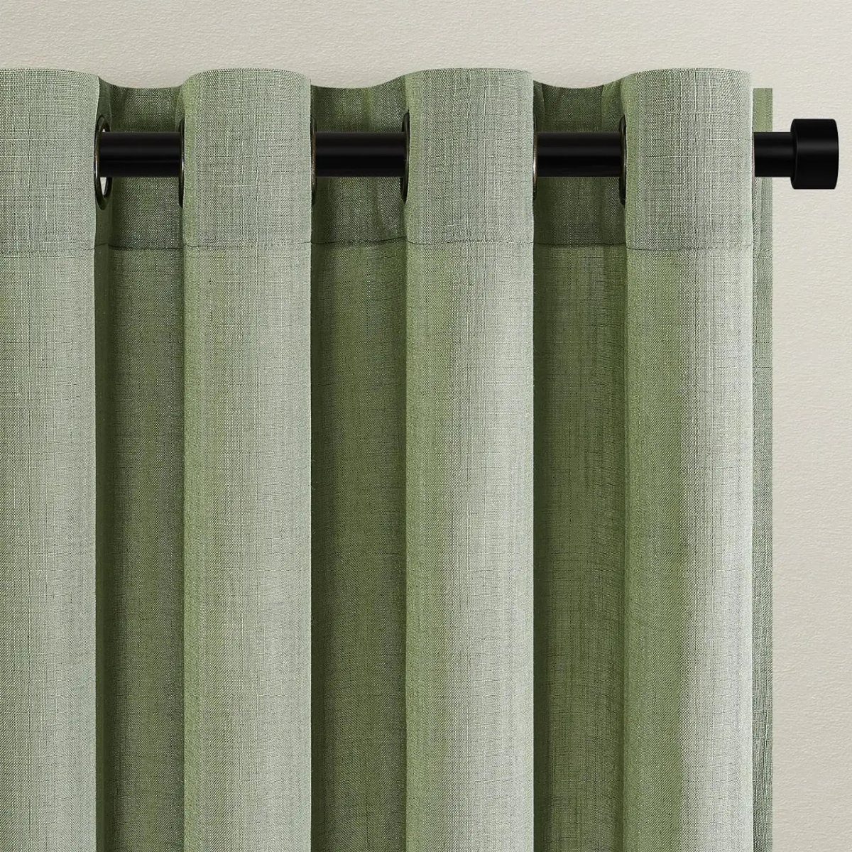 Sage green textured curtains hanging on a black metal rod against a light wall.