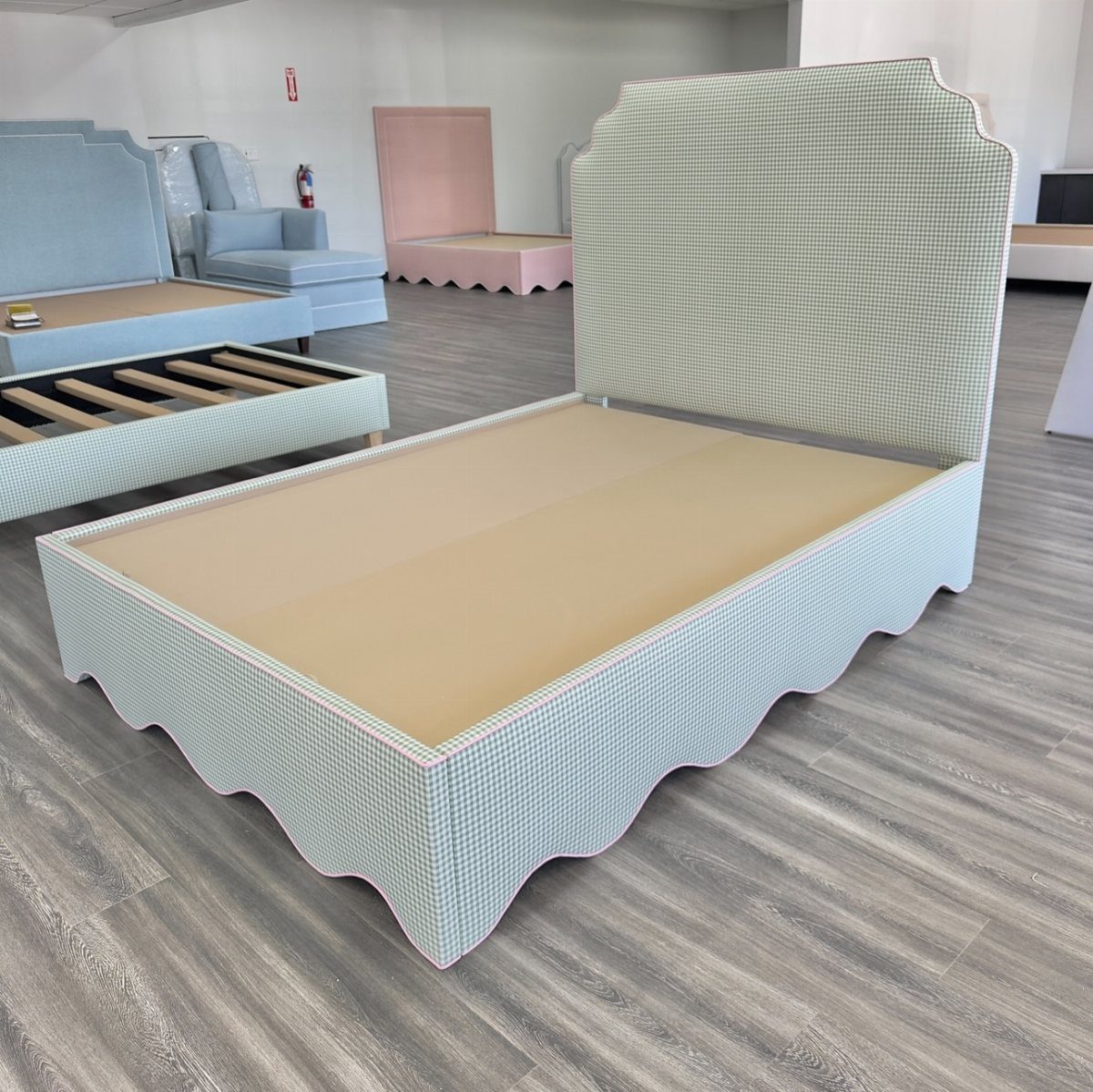 A light sage green upholstered bed frame featuring a tall scalloped headboard and a wavy base.