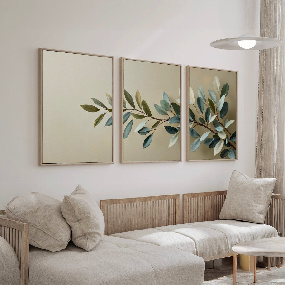 Three botanical leaf prints in wooden frames hanging above a beige sofa in a bright room.