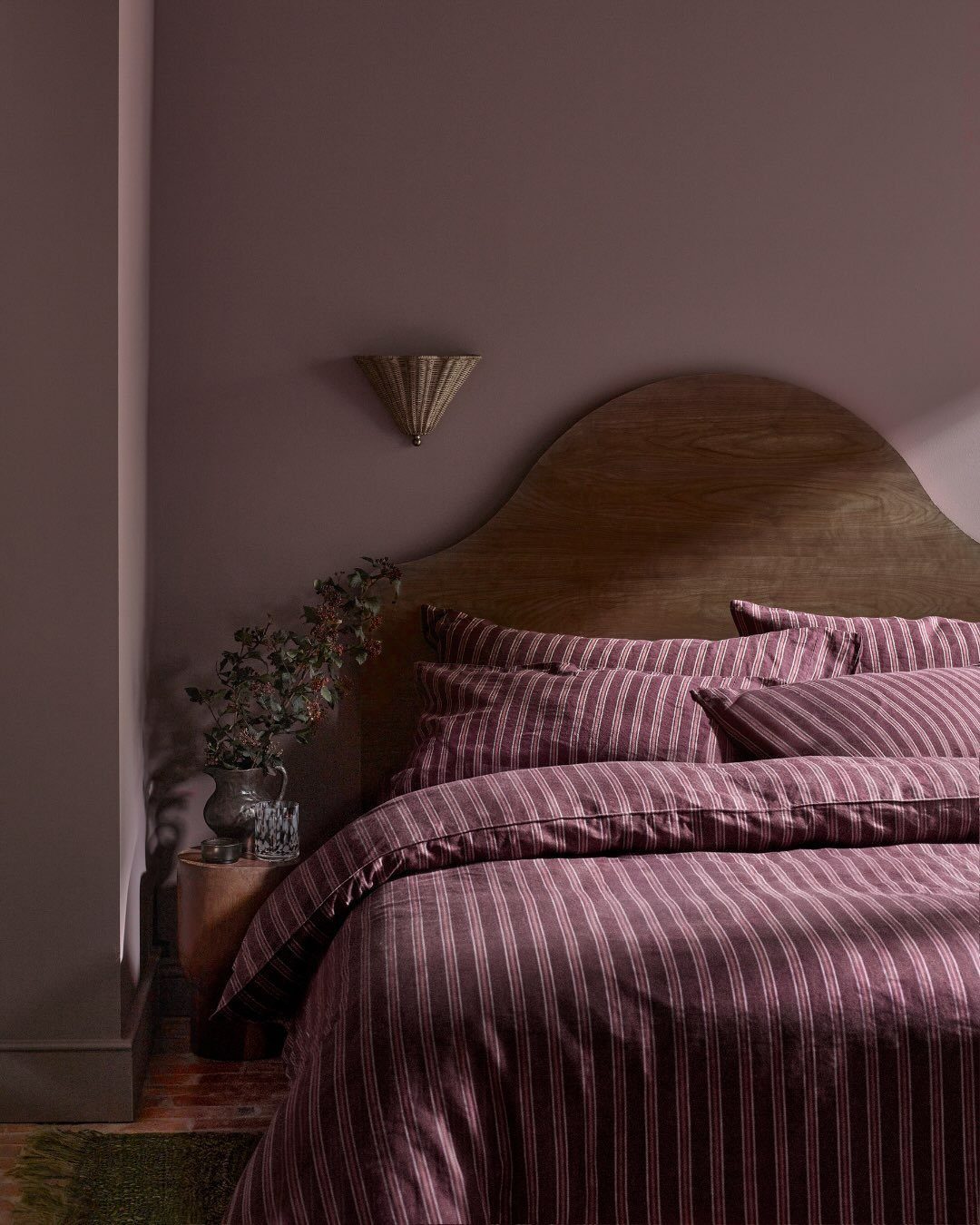Striped mauve bedding on a bed with a wooden arched headboard against a mauve wall.
