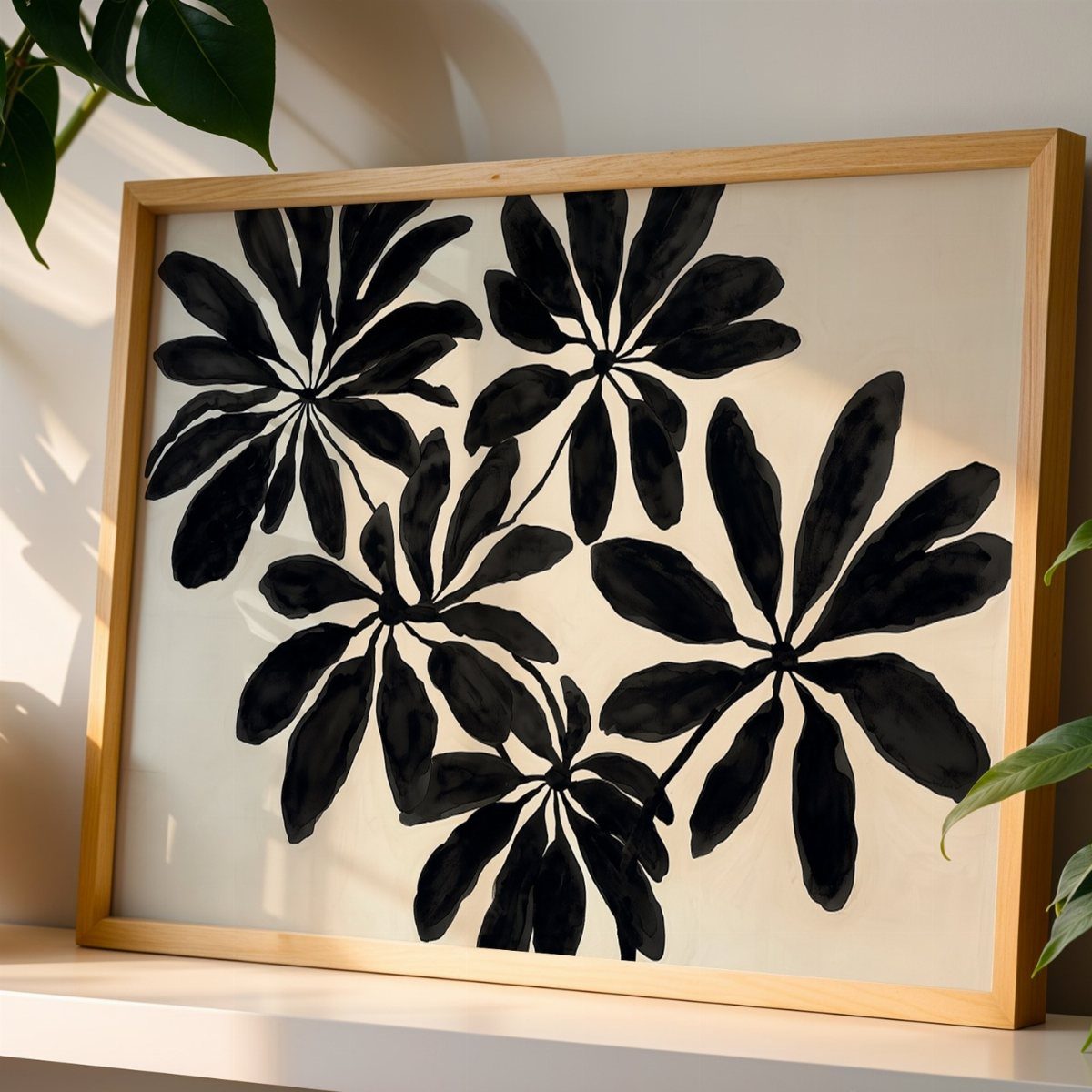 Black botanical leaf print in a light wood frame resting on a white shelf.