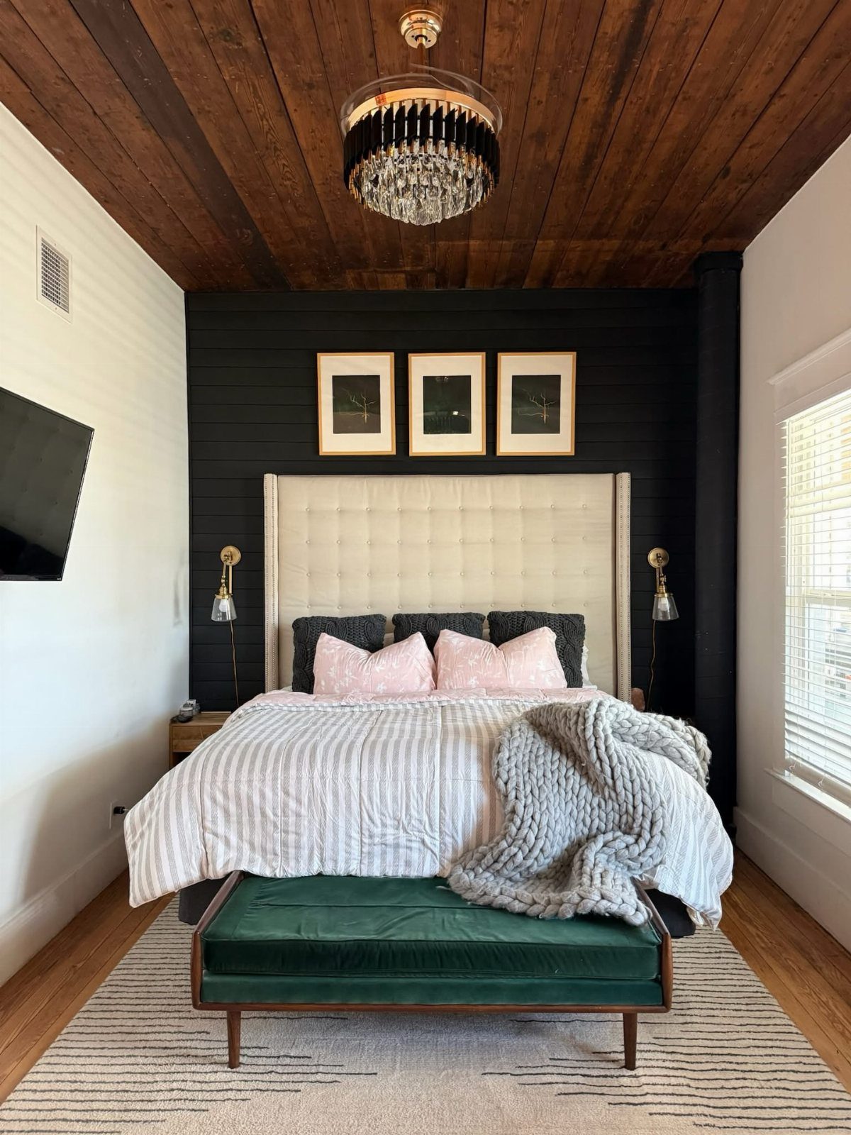 A modern bedroom with a tufted headboard, textured white bedding, pink pillows, and a dark accent wall.