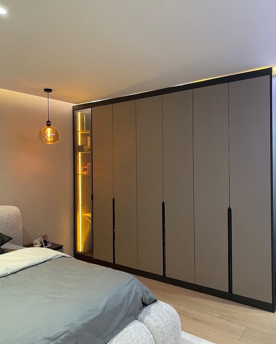 Minimalist grey wardrobe with black handles and warm lighting in a modern bedroom setting.