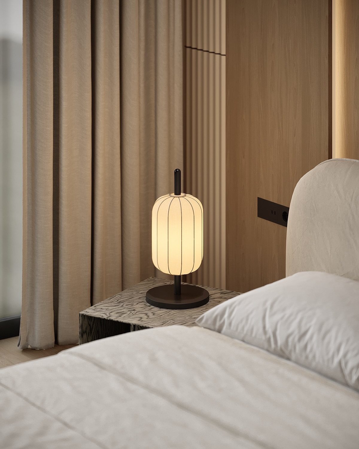 A modern ribbed table lamp glowing on a patterned nightstand next to a white bed.