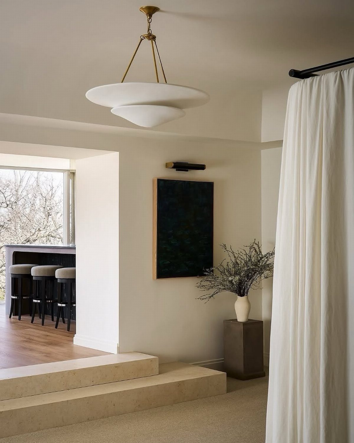 A large white tiered sculptural pendant light hanging from a gold rod in a minimalist room.