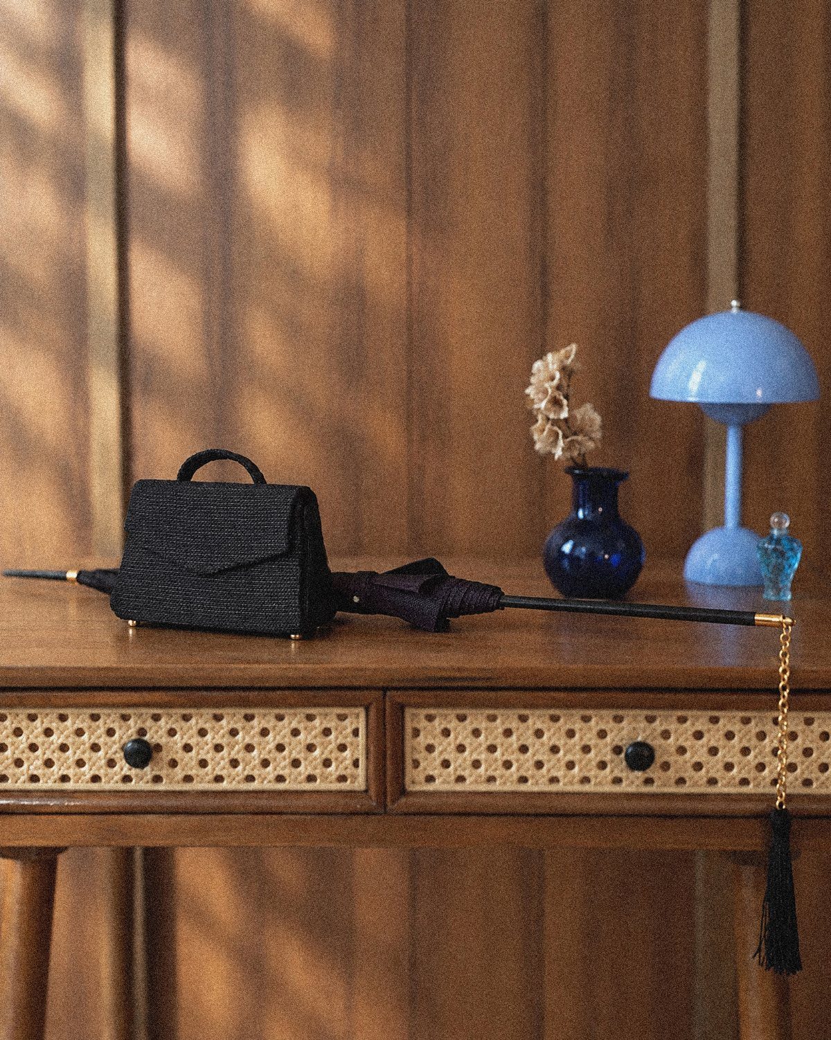 Personal items including a black handbag, umbrella, and blue decor arranged on a wooden dresser.