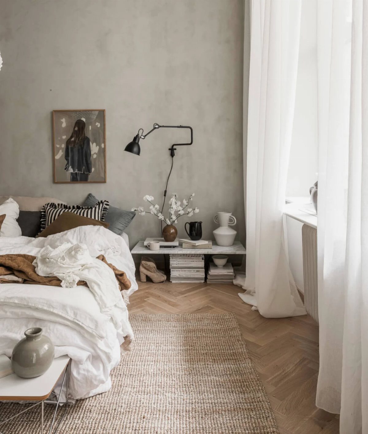A minimalist bedroom with white bedding, a grey textured wall, and light wood herringbone floors.