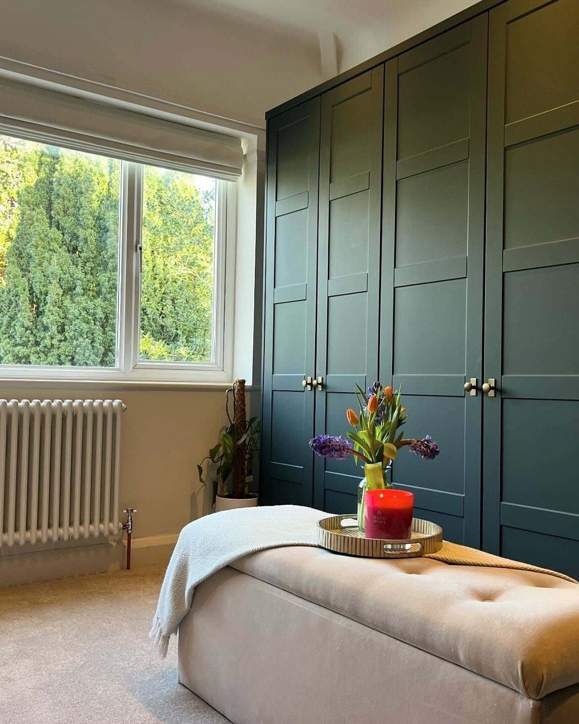 Dark green paneled wardrobes next to a large window with views of green trees.