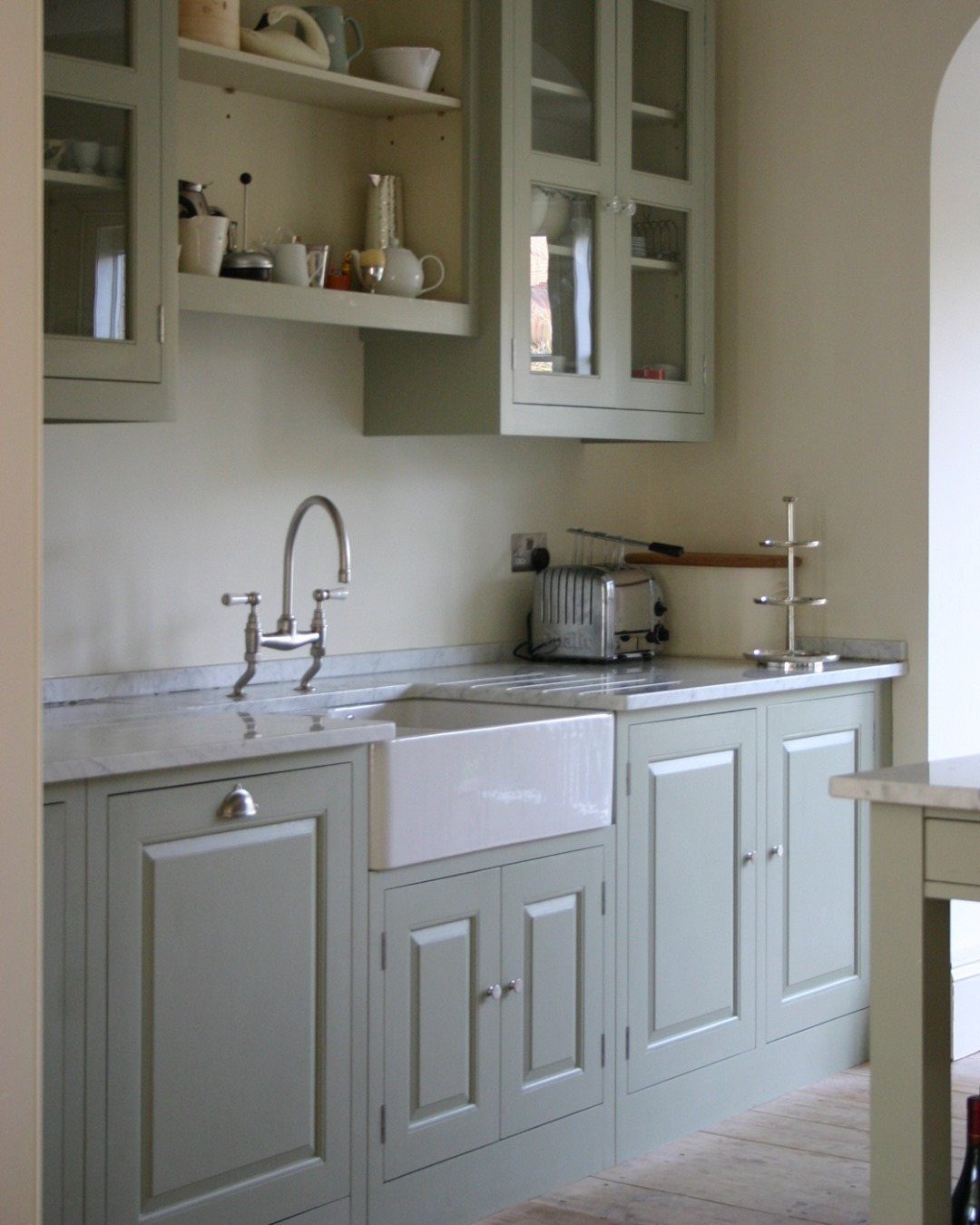 Sage green kitchen cabinets and open shelving above a white farmhouse sink.