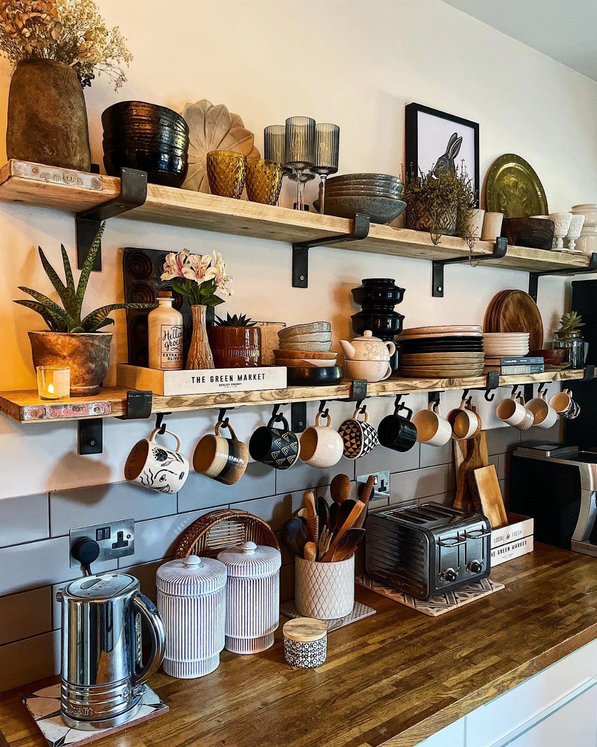 Wooden floating shelves decorated with vases, ceramics, glassware, and plants above a kitchen counter.