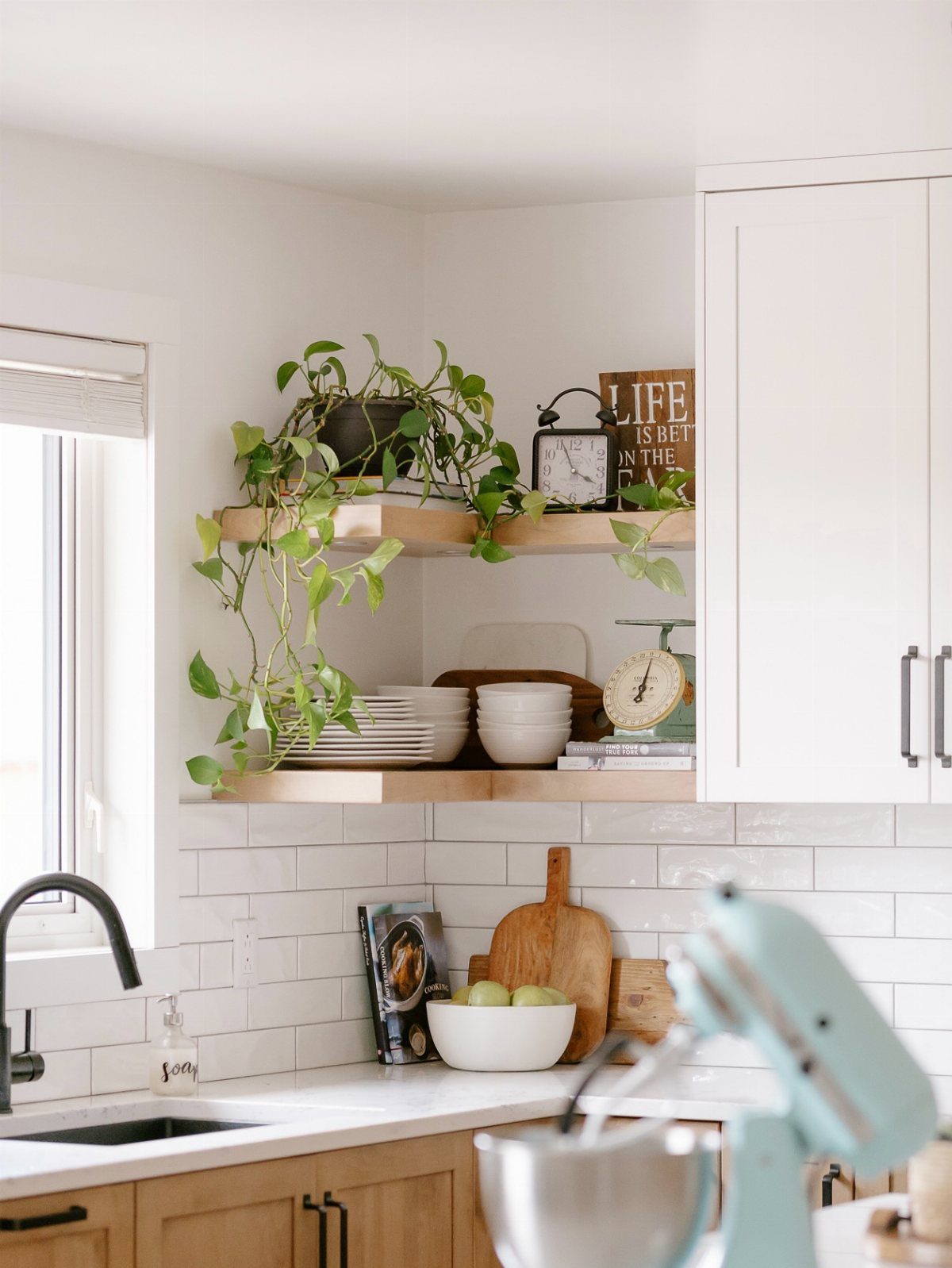 Wooden floating shelves in a kitchen corner holding white dishes and a trailing green plant.