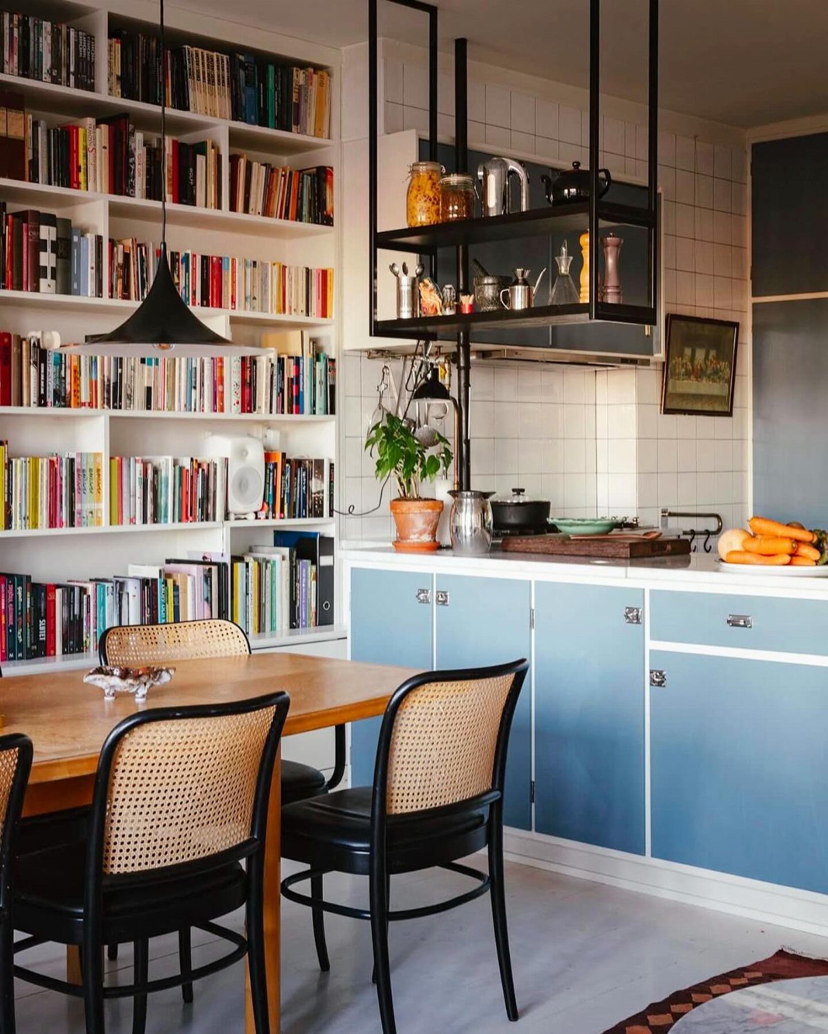 Large white built-in bookshelves filled with colorful books next to a blue kitchen cabinet setup.