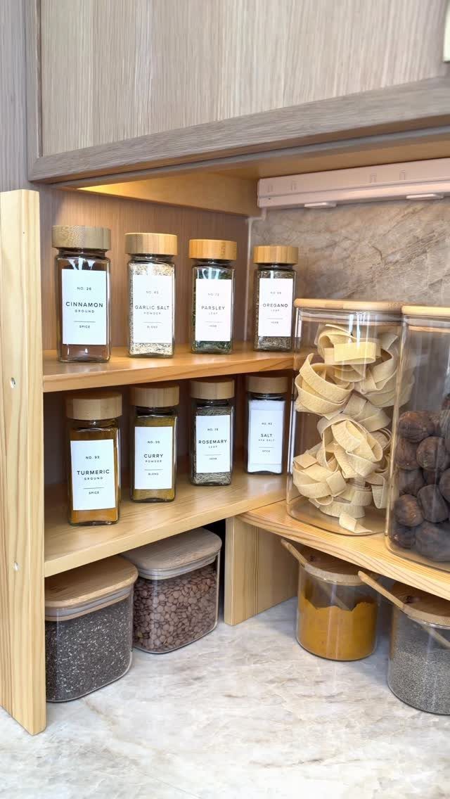 Glass spice jars and large pasta canisters arranged on light wooden kitchen shelves.