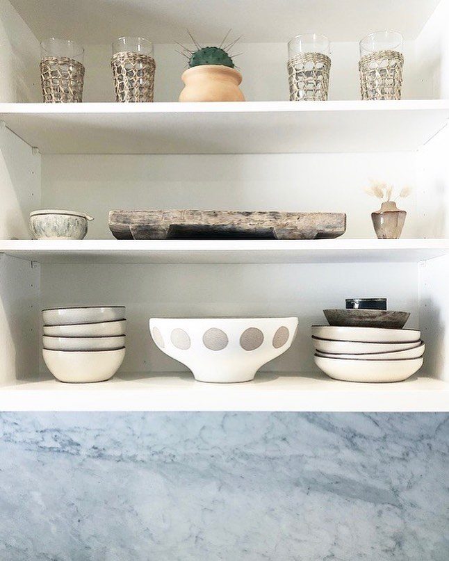 White floating shelves holding textured glassware, ceramic bowls, and a small cactus plant.