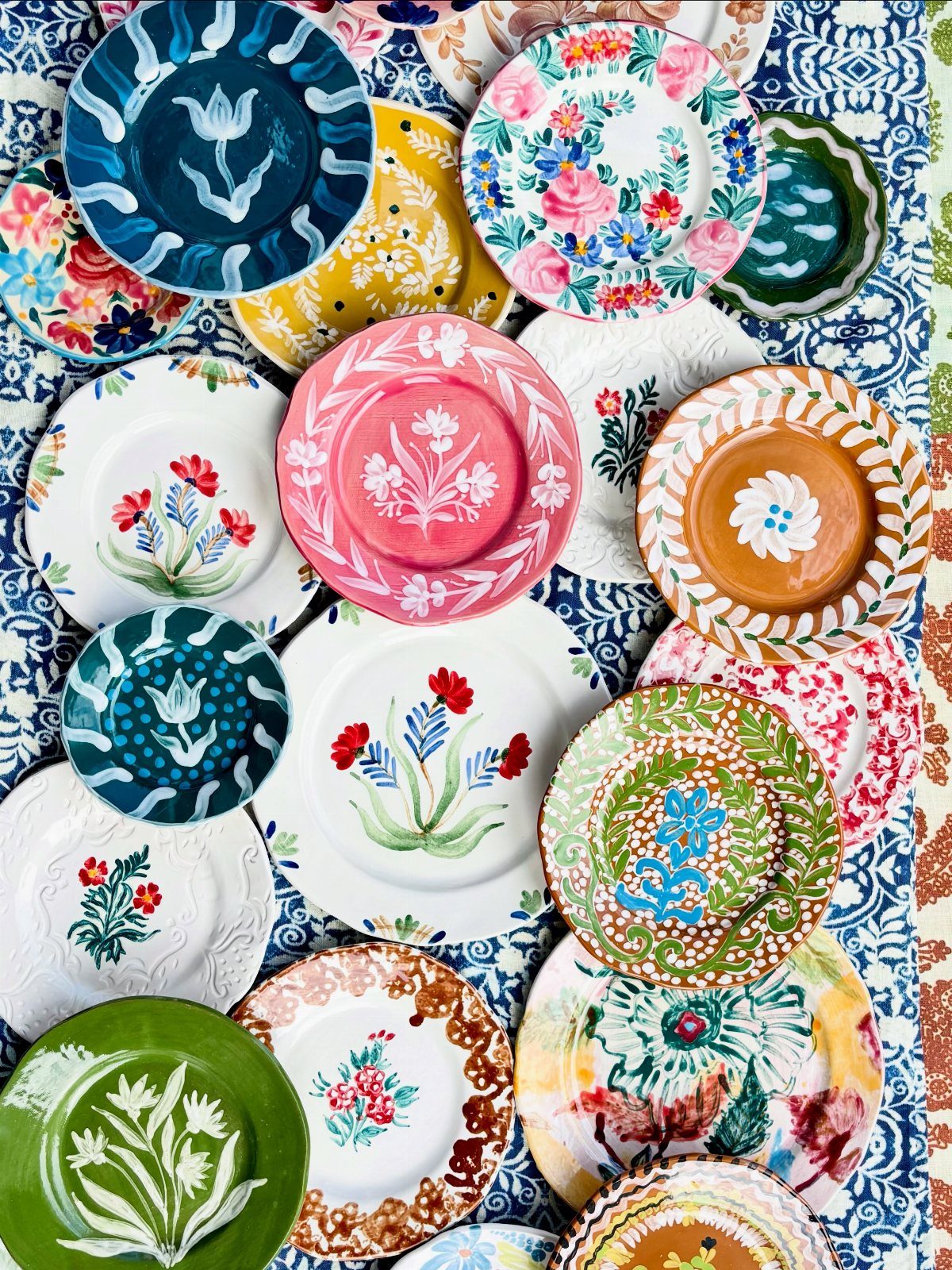 Various colorful patterned ceramic plates arranged on a blue and white patterned tablecloth.