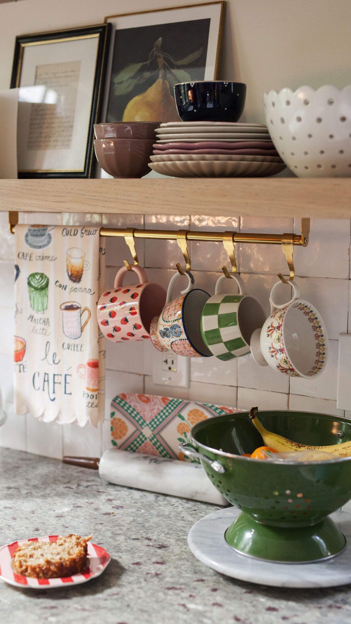 Colorful mugs hanging from a brass rail mounted under a wooden kitchen shelf.