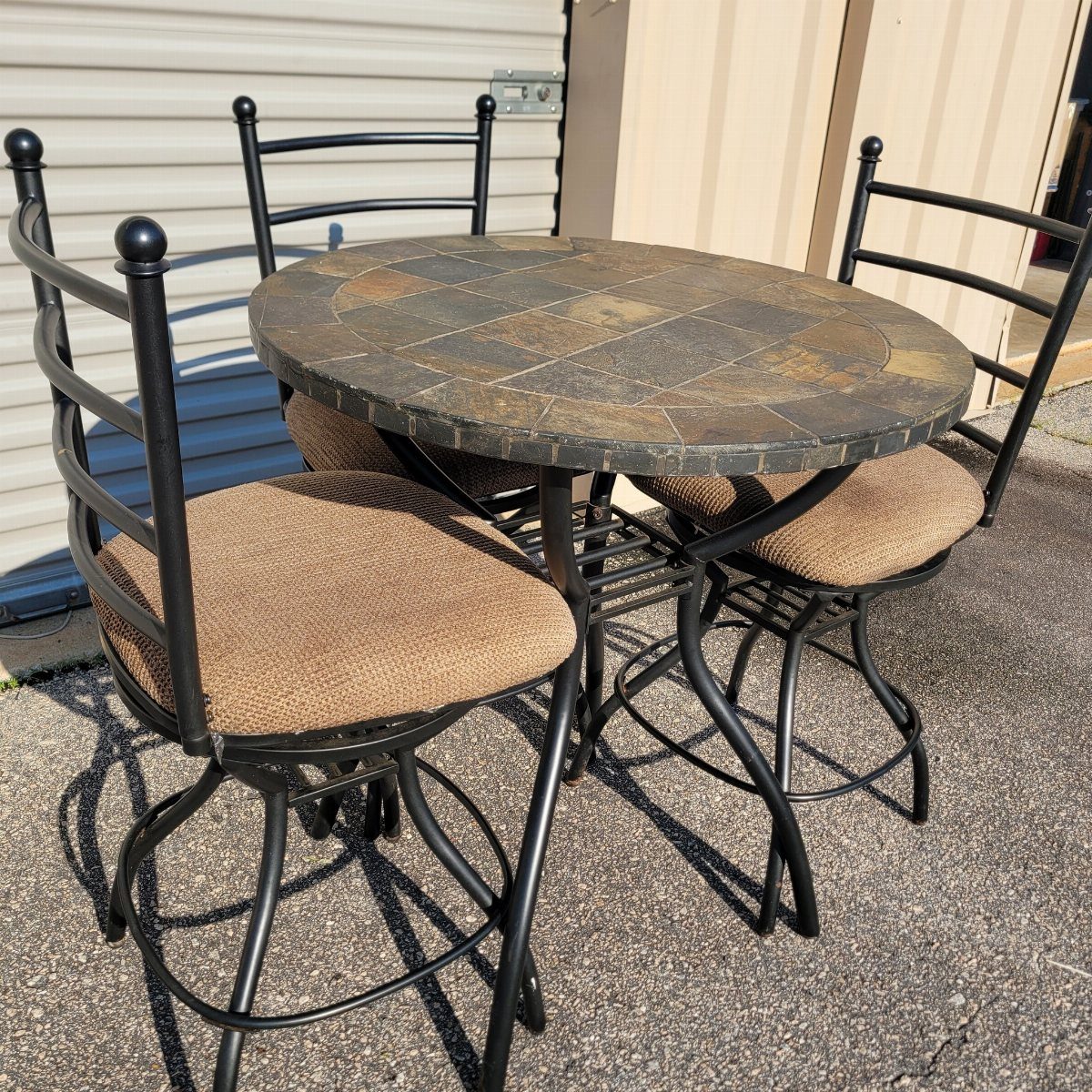 A small black metal bistro set with stone tabletop and tan cushioned chairs.