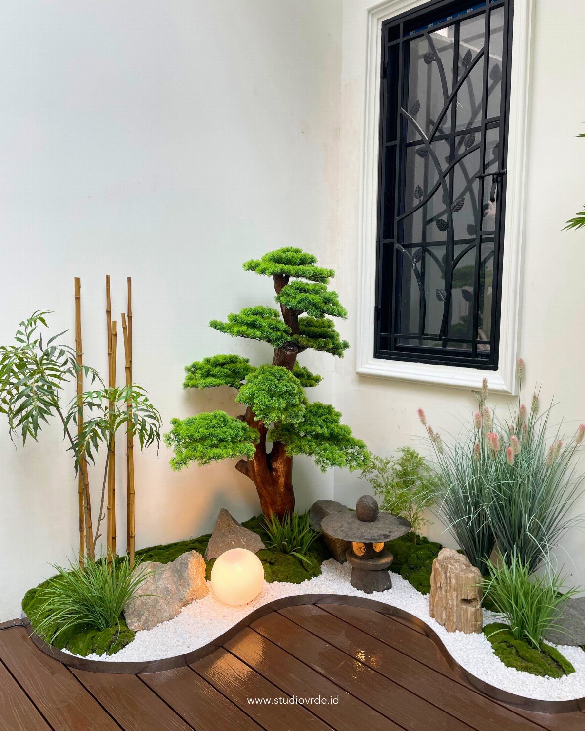 A miniature Zen garden with a bonsai tree, bamboo, and stone lantern on white gravel.