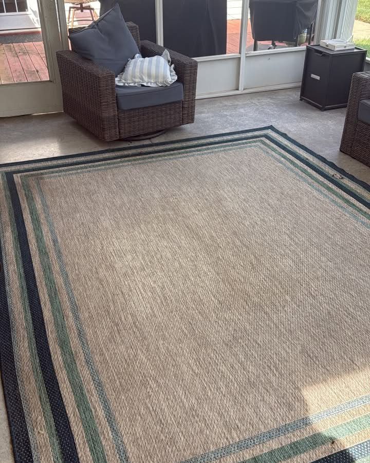 A large beige outdoor rug with blue and teal stripes on a patio.