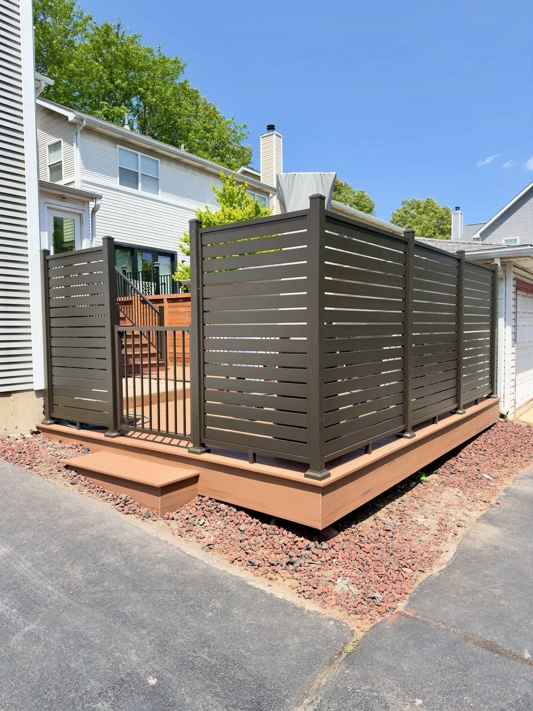 Dark brown horizontal slat privacy screen enclosing a small wooden deck area.