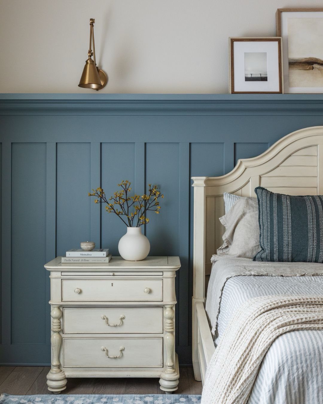 Blue board-and-batten wall paneling behind a white nightstand and a cream-colored bed in a bedroom.